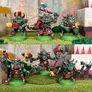 A group of five 28mm scale space orc miniatures is displayed, showcasing their vibrant colors and detailed designs. The top row features orcs in various poses, armed with weapons like a large axe and a futuristic gun, adorned with red and black armor and horned helmets. The bottom row presents another set of orcs, also equipped with axes and guns, emphasizing their fierce appearance with skull motifs and cybernetic enhancements. The backdrop includes a textured surface resembling a rocky terrain, enhancing the overall scene.