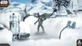 A Rebel Officer stands prominently in a snowy landscape, wearing a brown jacket and a red cap, with one hand raised as if giving orders. In the background, a detailed speeder truck and various mechanical structures are partially obscured by snow, creating a wintry atmosphere. The scene is set against a backdrop of distant mountains under a clear blue sky.