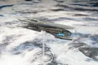 Grey spaceship model with blue lights on a clear stand against a cloudy background.