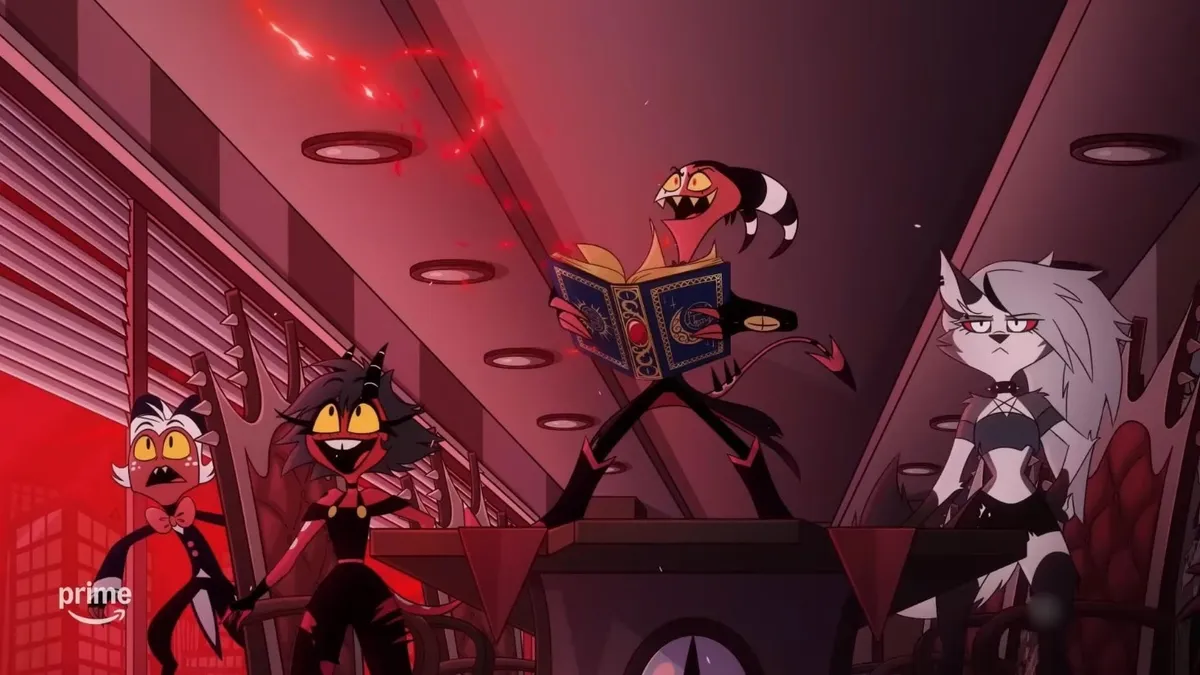 Two cartoon characters in a dimly lit, red-lit room. One stands on a desk reading an open book with ornate designs, wearing a black robe and pointed hat. The other, seated, has spiked hair, a black outfit, and a wide grin.