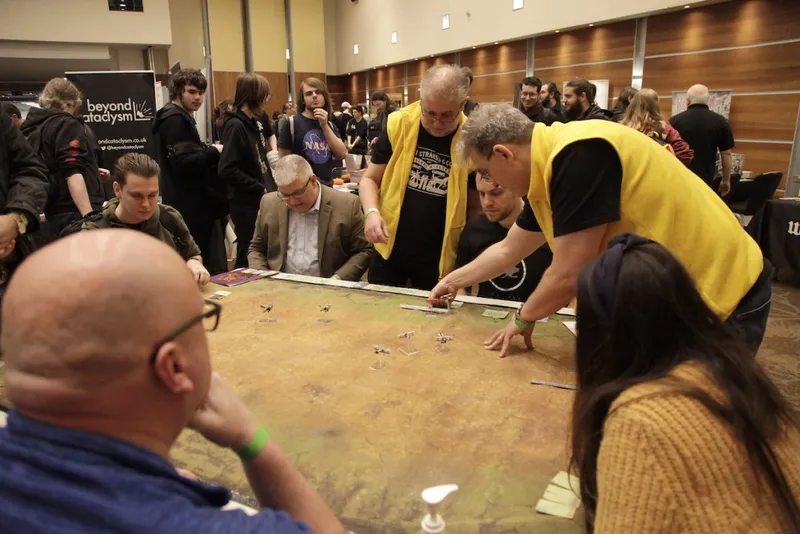 Group playing a tabletop game with miniatures on a large mat, indoors.