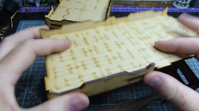 Hands holding a wooden MDF building piece with etched details.