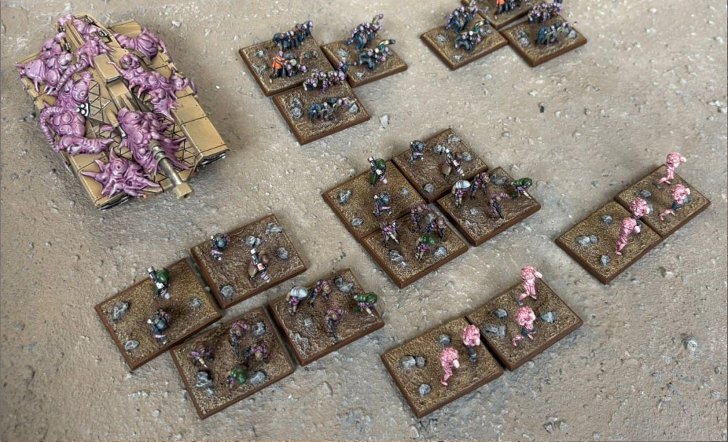 A collection of Zayken miniatures from Void Scar Miniatures is displayed on a textured surface. In the foreground, several bases feature hordes of zombified figures in various colors, including green, purple, and pink, representing the Neophyte Mobs. To the left, a tank is adorned with grotesque, bloated creatures, suggesting a fusion of machine and undead, while additional bases of zombies are scattered throughout the scene, emphasizing the overwhelming numbers of the Zayken forces.