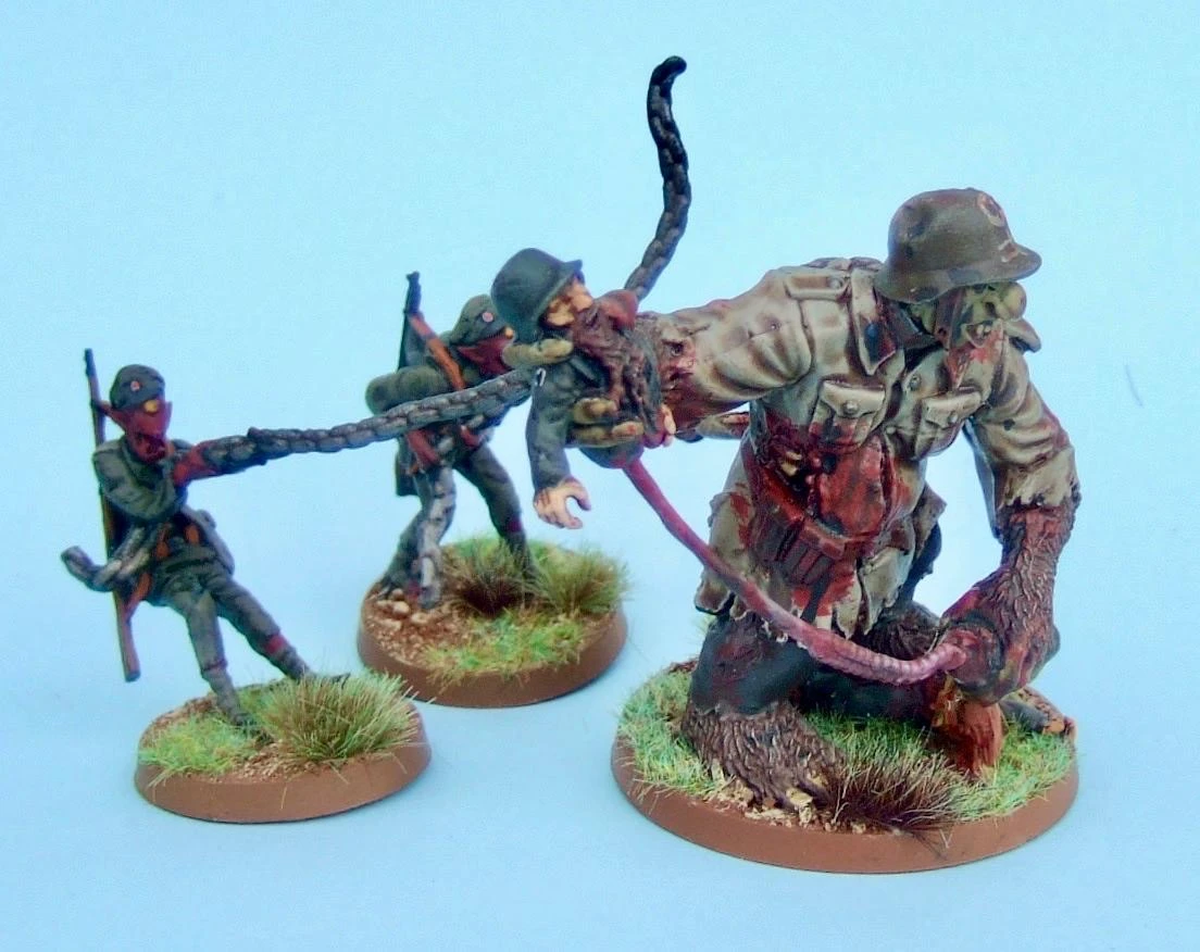 A trio of miniatures from the Panzerfäuste game is depicted, featuring two soldiers in dark uniforms and masks, each holding a weapon, and a larger, grotesque figure resembling a zombie or monstrous soldier. The larger figure has a tattered uniform and is being restrained by a long, tentacle-like appendage. The bases of the miniatures are painted in earthy tones with tufts of grass, set against a light blue background.