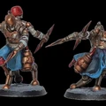 Two intricately designed miniatures from the game VoidSeige are displayed, showcasing a warrior in armor with a bronze finish and a blue tunic. Each figure is posed dynamically, holding a spear in one hand while the other arm is extended, suggesting movement. The miniatures are mounted on circular bases, with a textured surface that adds to their detailed appearance.