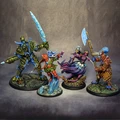 Four intricately designed miniatures from the underwater tabletop skirmish game DeepWars are displayed against a neutral background. On the left, a large, armored figure with a green and blue color scheme wields a large ice sword. Next to it, a humanoid character in vibrant red and green attire gestures dramatically, showcasing blue skin and a confident expression. The third figure, a mermaid-like character with flowing purple hair and a shimmering tail, holds a staff adorned with a glowing orb. On the right, a warrior with a blue head and patterned armor brandishes a large axe, completing the diverse ensemble of characters. Each miniature is mounted on a textured base that reflects an underwater theme.