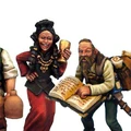 Three detailed miniatures are depicted, representing characters typically found in a fantasy tavern. On the left, a man carries a large barrel and two jugs, wearing a simple tunic and trousers. In the center, a woman in a vibrant red dress holds a goblet and smiles, adorned with jewelry. On the right, a bearded man with a backpack is reading from an open book, dressed in a light shirt and trousers.