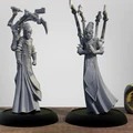 Two detailed 3D printed miniatures stand on black bases, showcasing the Cephalyx Mind Slayers from the Warmachine universe. Each figure is dressed in long, flowing robes and features a distinctive mask, with one holding a pair of mechanical arms equipped with weapons, while the other has its hands clasped in a gesture of focus. The background is a simple gradient, emphasizing the intricate designs of the miniatures, with a decorative die featuring a symbol from the game placed nearby.