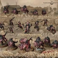 A dynamic scene showcases a variety of new Khornate miniatures set against a desolate, skull-laden landscape. Central to the composition is the Deathbringer, a formidable warrior adorned in dark armor, wielding a massive axe and a spiked shield, flanked by several Flesh Hounds and their three-headed alpha, Karanak. Surrounding them are additional warriors, all intricately detailed and painted in shades of red and black, emphasizing their menacing presence in this chaotic battlefield.