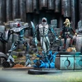 A detailed scene showcases several miniatures from the Star Wars: Shatterpoint game. In the foreground, a Quarren character stands on a base with blue, swirling water effects, while a humanoid figure in a gray suit, holding a weapon, is positioned nearby. To the left, a droid with a sleek design and red accents is poised, and in the background, a second droid stands ready for action against a backdrop of rocky terrain and structures, enhancing the dynamic atmosphere of the scene.