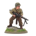 A 28mm scale miniature of a soldier, representing the war hero Audie Murphy, stands on a rocky base adorned with green grass. The figure is dressed in a light green military uniform with insignia on the sleeves and wears a helmet. He holds a machine gun in a ready position, showcasing a determined expression.