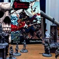 A vibrant tabletop scene features the rulebook for "Boarders and Black Flags" by Man ’o’ Kent Games, prominently displayed in the center. The cover art depicts a dynamic pirate battle on a ship, with characters wielding swords and engaging in combat. Surrounding the book are several unpainted miniatures, including human pirates and undead Skelliwags, set against a backdrop of MDF scenery elements like masts and crates, all arranged on a wooden table.
