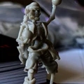 A detailed miniature of a skeleton pirate stands with one arm raised, holding a round object, possibly a cannonball or a drink. The figure is intricately sculpted, showcasing skeletal features and pirate attire, including tattered clothing. The background is slightly blurred, revealing stacks of game-related materials, suggesting a tabletop gaming environment.