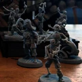 A collection of detailed miniatures from the game "Boarders and Black Flags" features a mix of human pirates and undead skeletons. The pirates are depicted in dynamic poses, some wielding swords and others holding various pirate-themed accessories, showcasing their character and personality. In the background, a wooden structure resembling a ship's deck adds context to the scene, enhancing the overall pirate theme.