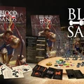 A dynamic display of the game "Blood on the Sands" features a prominent cover illustration of a gladiator in armor, wielding a sword, set against a backdrop of an arena. Surrounding the central image are various game components, including a reference guide, character cards, tokens, and a sprue of miniatures, all laid out on a sandy surface. The title "BLOOD ON THE SANDS" is boldly presented at the top, emphasizing the game's focus on gladiatorial combat.