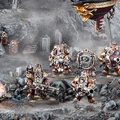 A group of Kharadron Overlords, depicted as flying dwarves in intricate nullsuits, stands on a rocky terrain. They are equipped with various steampunk-inspired weapons and gadgets, showcasing a mix of bronze and metallic colors. In the background, an airship hovers above, adding to the adventurous atmosphere of the scene.