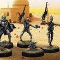 A group of four miniatures from the Star Wars universe is displayed against a desert backdrop featuring a simple structure. On the left, a character in a silver and black armor, resembling a bounty hunter, stands confidently. Next to him, two IG-Series Assassin Droids are posed with weapons drawn, showcasing their metallic bodies and intricate details. In the foreground, Grogu, a small figure with large ears, is depicted holding a small object, adding a whimsical touch to the scene. The ground is textured with grass and dirt, enhancing the overall aesthetic of the miniatures.