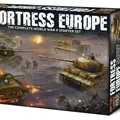 A box for the "Fortress Europe" starter set for the Flames Of War wargame prominently displays the title in bold, distressed lettering. The artwork features a dynamic battlefield scene with American and German forces, including tanks and soldiers engaged in combat. The background showcases a smoky, war-torn landscape, enhancing the theme of World War II wargaming.