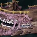 A detailed model of a sailing ship designed to resemble a mimic, featuring a large, gaping mouth with sharp teeth at the bow. The ship's body is textured with a mix of wood and fleshy elements, showcasing a pinkish hue and various grotesque features, including additional smaller mouths and eyes. The deck is adorned with a wooden railing and a central mast, emphasizing its fantastical and eerie design.