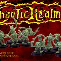 A collection of hand-sculpted miniatures from beQuest Miniatures is displayed, featuring various chaotic critters in dynamic poses. The miniatures are cast in a green material and are set against a dramatic red background, with the title "Chaotic Realms" prominently featured in a bold, stylized font. The beQuest logo is visible in the lower left corner, adding to the overall thematic presentation.