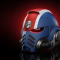 A wearable Space Marine helmet features a striking design with a blue and red color scheme, accented by a prominent skull emblem on the forehead. The helmet has a sleek, angular shape with dark eye lenses and ventilation grills on the front. It is set against a dramatic dark red background, enhancing its imposing appearance.