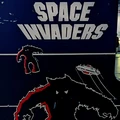 A close-up of an arcade cabinet featuring the classic game "Space Invaders." The cabinet is predominantly dark blue, with bold white lettering spelling out "SPACE INVADERS" at the top. Below, stylized graphics depict a menacing alien creature in black and red, along with a spaceship firing projectiles, capturing the retro aesthetic of early video gaming. The overall design evokes nostalgia for the arcade era.
