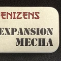 A small, silver tin features the text "DENIZENS" in bold red letters at the top and "EXPANSION MECHA" in large, black, stencil-style font below. The tin's surface has a smooth, metallic finish, and it is set against a dark background, emphasizing its compact and portable design. This packaging represents the new expansion for the Space Denizens wargame, which includes mechs and terrain features.