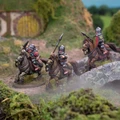 Three mounted halfling cavalry figures are depicted, each riding stout ponies and equipped with spears. The riders wear armor and helmets, showcasing a mix of colors, including silver and red accents. The scene is set in a lush, grassy landscape with rocky terrain and a distant background of rolling hills, creating a vibrant and dynamic atmosphere.
