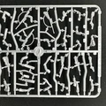 A plastic sprue featuring various components for miniature figures, including torsos, limbs, and heads, designed for 28mm scale modern civilians and post-apocalyptic survivors. The sprue showcases a variety of poses and accessories, including weapons, allowing for customization of the miniatures. The pieces are molded in a light gray plastic and are arranged in a grid pattern on a black background.