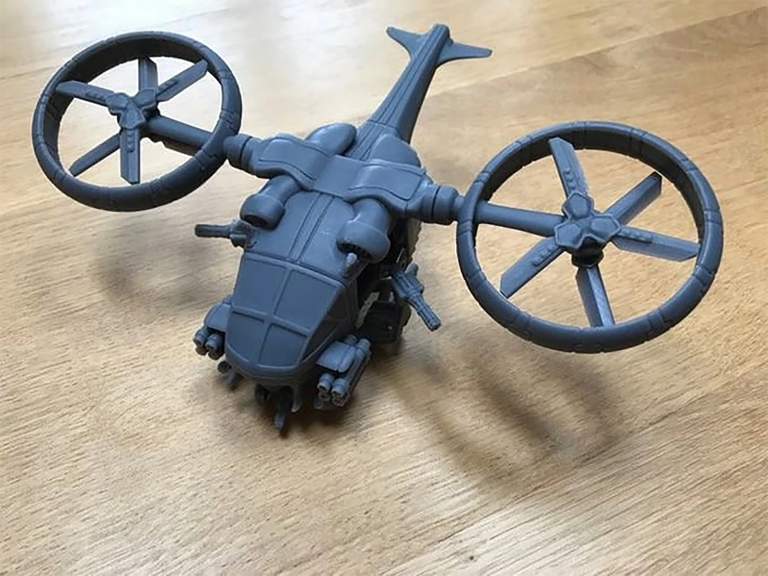 A gray, unpainted model of the LARC 2, a sci-fi VTOL aircraft, is displayed on a wooden surface. The model features two large, circular anti-grav rotors mounted on either side, a streamlined body with a detailed cockpit area, and various protruding components that suggest modularity for different configurations. The design includes a chin mount hardpoint and twin rotor assemblies, emphasizing its futuristic utility and adaptability.