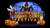 A vibrant graphic features the text "MANCHESTER BOARD GAME FESTIVAL" prominently displayed in bold, orange letters against a dark, spooky backdrop. The scene includes a haunted house with glowing windows, bats flying in the night sky, and various Halloween-themed elements like pumpkins, skulls, and spider webs. The overall atmosphere is festive and eerie, perfectly capturing the Halloween spirit of the event.