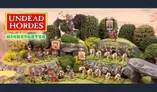 The scene features a vibrant tabletop display showcasing the "Undead Hordes" miniatures from Red Bard Games' Kickstarter campaign. In the foreground, a variety of skeletons and zombies are arranged on grassy terrain, with some holding banners and others in dynamic poses. A prominent liche king rides a zombie dragon atop a rocky outcrop, while additional figures, including a necromancer and various undead warriors, populate the scene, surrounded by lush greenery and stone formations. The overall composition exudes a classic fantasy aesthetic, emphasizing the theme of an undead army ready for battle.
