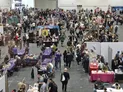 Crowded convention hall with people browsing vendor booths and gaming tables.