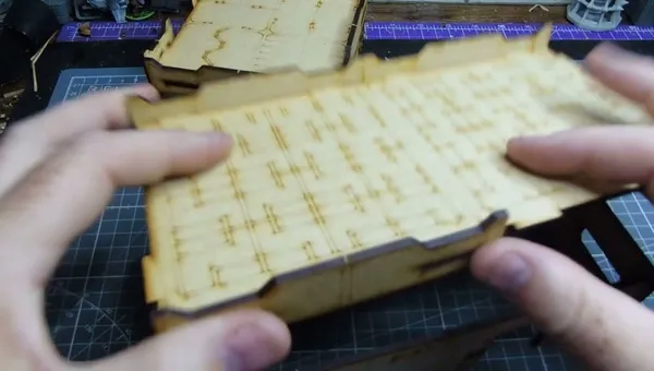 Hands holding a wooden MDF building piece with etched details.