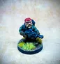 A detailed miniature of a rugged space dwarf stands in a dynamic pose, holding a futuristic weapon. He wears a red bandana, a green jacket, and has a scruffy beard, conveying a tough, battle-ready appearance. The base features tufts of green grass, enhancing the jungle theme, against a softly blurred background.