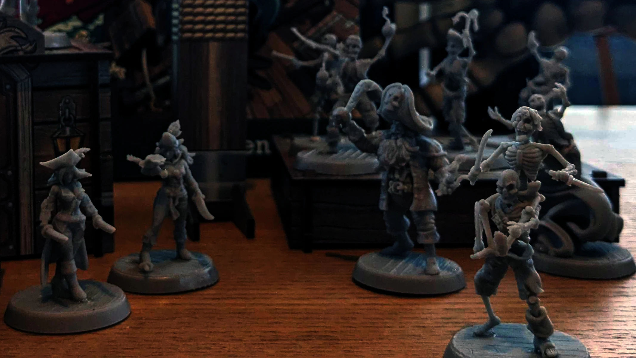 A collection of detailed miniatures from the game "Boarders and Black Flags" features a mix of human pirates and undead skeletons. The pirates are depicted in dynamic poses, some wielding swords and others holding various pirate-themed accessories, showcasing their character and personality. In the background, a wooden structure resembling a ship's deck adds context to the scene, enhancing the overall pirate theme.