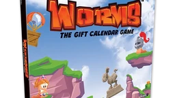 A colorful box for "Worms: The Gift Calendar Game" features a vibrant illustration of cartoonish landscapes with green hills and rocky cliffs. Prominent characters include a pink worm wearing a crown and a knight, both positioned on the cliffs, while a hot air balloon floats in the sky. The title is boldly displayed at the top, emphasizing the festive theme of the advent calendar.