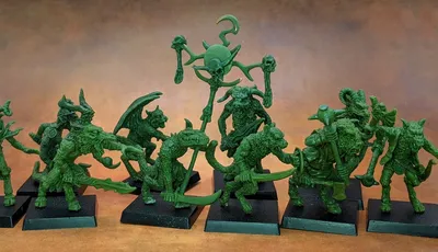 A collection of old school miniatures from Satyr Art Studio, featuring various fantastical creatures in a vibrant green color. The figures include beastmen with distinct features such as horns and claws, some wielding weapons, and a central figure holding a staff topped with a skull and a crescent. They are displayed on black bases against a warm, textured background.