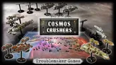 Miniature wargame scene with space-themed terrain featuring small metallic ships and structures on a purple-hued battlefield. Text reads "COSMOS CRUSHERS" on a central metallic plaque and "Troublemaker Games" at the bottom.