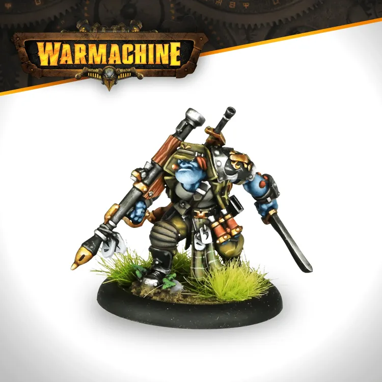A trollkin warrior stands confidently, equipped with a large firearm slung over one shoulder and a sword in hand. He has blue skin, wearing a mix of tactical gear and armor, with various pouches and tools attached to his outfit. The base features green grass, adding to the natural jungle theme, while the Warmachine logo is displayed prominently at the top of the image.