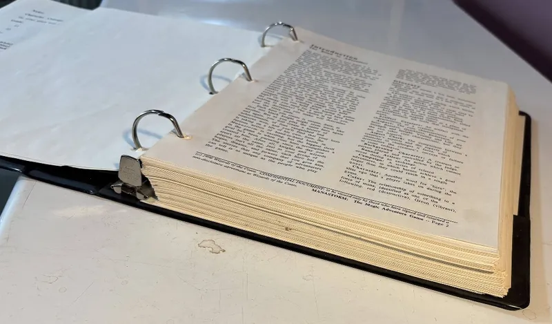 A three-ring binder filled with printed pages, showcasing the playtest manuscript for "ManaStorm: The Magic Adventure Game." The pages are slightly yellowed, indicating age, and feature text in a standard font, with some pages showing visible formatting and layout typical of tabletop RPG materials. The binder is resting on a flat surface, with the edges of the pages visible, suggesting a substantial amount of content within.