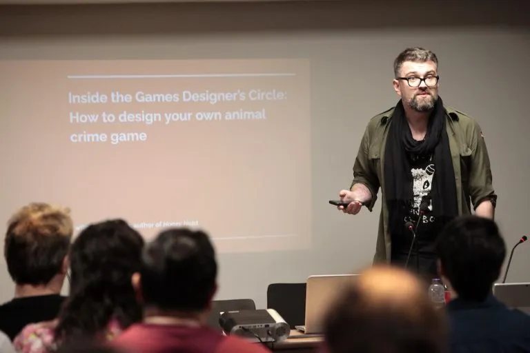 Man presenting to audience, slide reads "Inside the Games Designer's Circle: How to design your own animal board game"