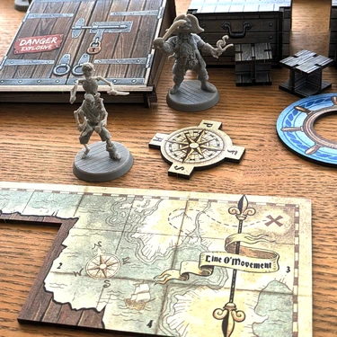 Two pirate miniatures are prominently displayed on a wooden table: one is a skeletal figure with a sword, and the other is a pirate with a tricorn hat and a hook for a hand. Nearby, a compass rose and a game board section titled