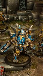A group of Cygnar miniatures is depicted in a detailed tabletop setting, showcasing the Gravedigger Auxiliaries unit. In the foreground, a character heavy warjack named Beaker stands prominently, adorned in blue and gold armor, with various mechanical features. Surrounding it are several elite veterans, including a female commander with red hair and a rifle, an ogrun captain, and a unit of Gravedigger Commandos, all featuring a mix of blue and gold uniforms, set against a backdrop of stone steps and a weathered door.