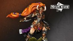 Kishtaar the Conqueror is depicted as a fierce warrior in ornate brass-faced armor adorned with intricate details and horned accents. She has long, flowing orange hair and stands confidently on a textured base with patches of grass. The figure is posed dynamically, holding a weapon in one hand, emphasizing her role as a powerful leader in the Warmachine universe. The name "KISHTAAR THE CONQUEROR" is displayed prominently at the bottom of the image.