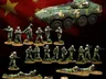 A collection of miniature figures representing China's People's Liberation Army (PLA) is displayed against a backdrop of the Chinese flag. The set includes various contemporary infantry soldiers in camouflage uniforms, special operations troops, and unmanned ground vehicles (UGVs). A prominently featured armored vehicle is also present, alongside soldiers in different poses, some standing with weapons, others in prone positions, and two quadruped UGVs positioned on the ground.