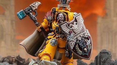 A dynamic miniature of Darnath Lysander in bright yellow Terminator armour, holding the relic storm shield Rampart in one hand and the Fist of Dorn power hammer in the other. His expression is fierce, and he wears a flowing cape, with intricate details on his armour and shield, including the name "LYSANDER" and various symbols. The background features a dramatic, fiery sky, enhancing the imposing presence of the character.