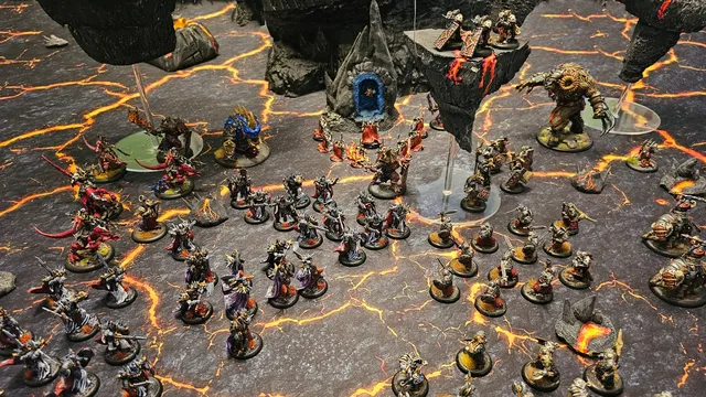 Miniature dark fantasy wargame scene with two armies on a cracked, lava-like battlefield. Left side features dwarven figures with armor and weapons, including a large blue-robed figure with a glowing orb.