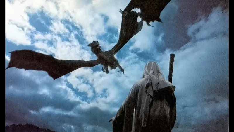 A dragon flying over a hooded figure holding a staff against a cloudy sky.