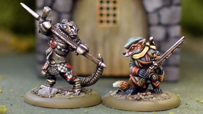 A fierce anthropomorphic badger in armor wields a large weapon, standing on the left, while a cunning-looking fox in a green hat and coat stands on the right, holding a small object. Both miniatures are detailed and painted, set against a blurred background of a stone structure with a wooden door. The scene captures the whimsical yet combative spirit of the Burrows and Badgers game.